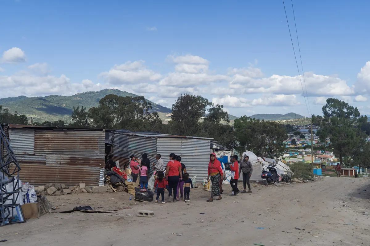 Familias reunidas frente a casas de lámina en una comunidad, con cerros al fondo